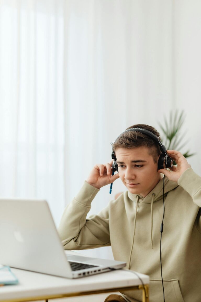 Teenage boy using headphones and laptop for online learning at home.